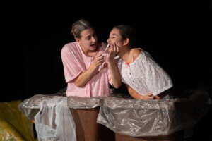 Foto promocional de l'obra Tribut de les rates. Dues dones vestides amb bates d'estar per casa es fan una prova de la Covid amb els bastonets al nas.