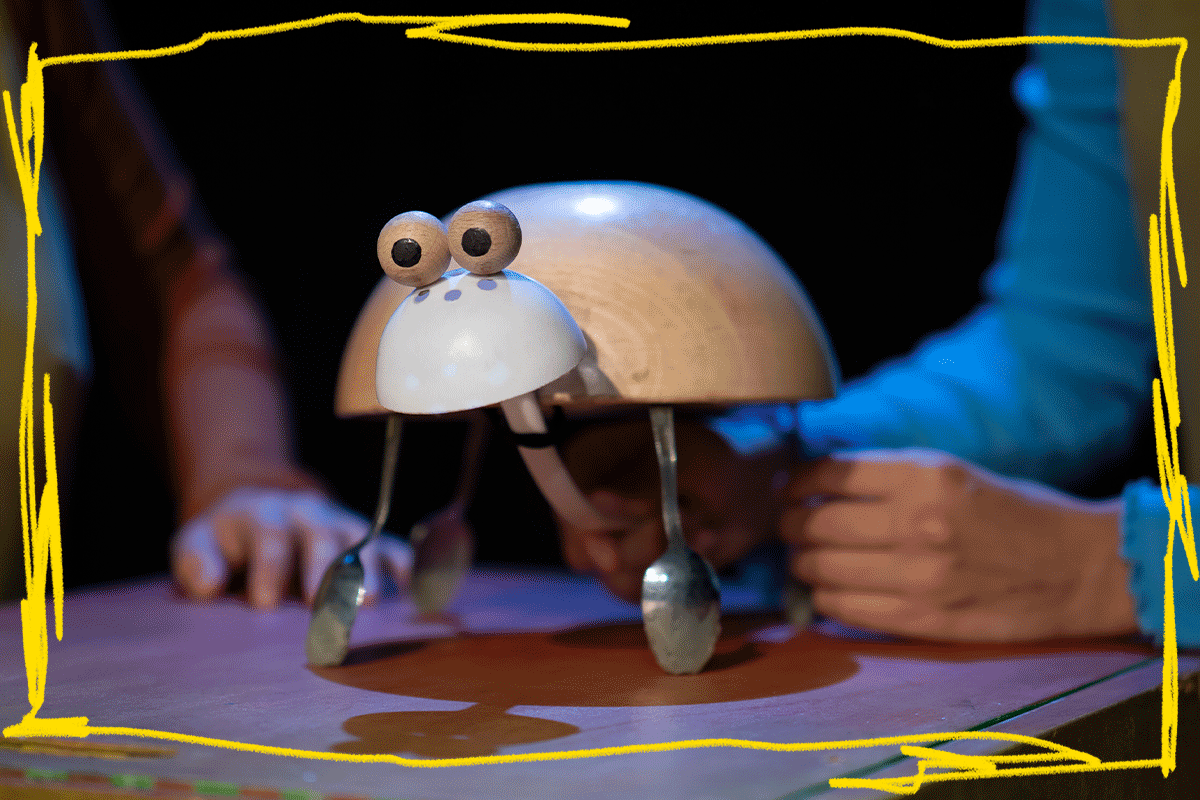 Foto promocional de l’espectacle escolar ‘Mal de closca”. Una titella amb forma de tortuga feta amb culleres, bols i boletes de fusta és manipulada per unes mans.