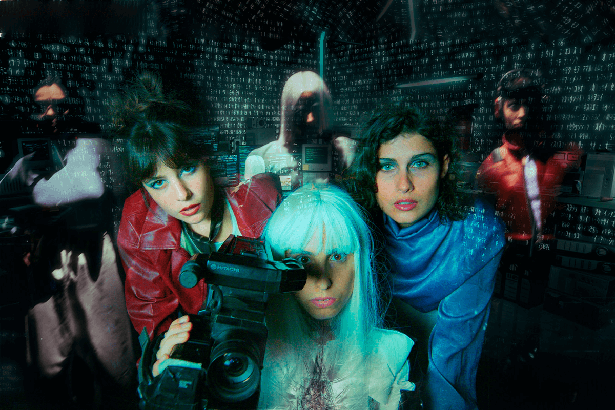 Foto promocional Mary’s Room black box. Sobre un fons fosc tres dones en primer pla. Dues al darrere, una amb cabells foscos, curt i una cua alta, vestida amb una jaqueta de cuir vermell, l’altra amb cabells foscos curts i arrissats amb una camisa blava metàl·lica, i al front, una dona amb els cabells blancs, llisos i llargs i un mono de cuir sintètic de color negre amb franges blanques amb una càmera de vídeo.